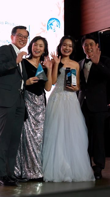 Video frame: four people smiling and waving on stage holding awards